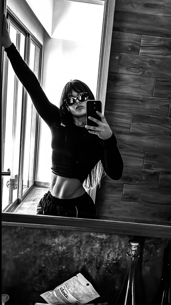 Coach taking a mirror selfie, posing to show off her abs.